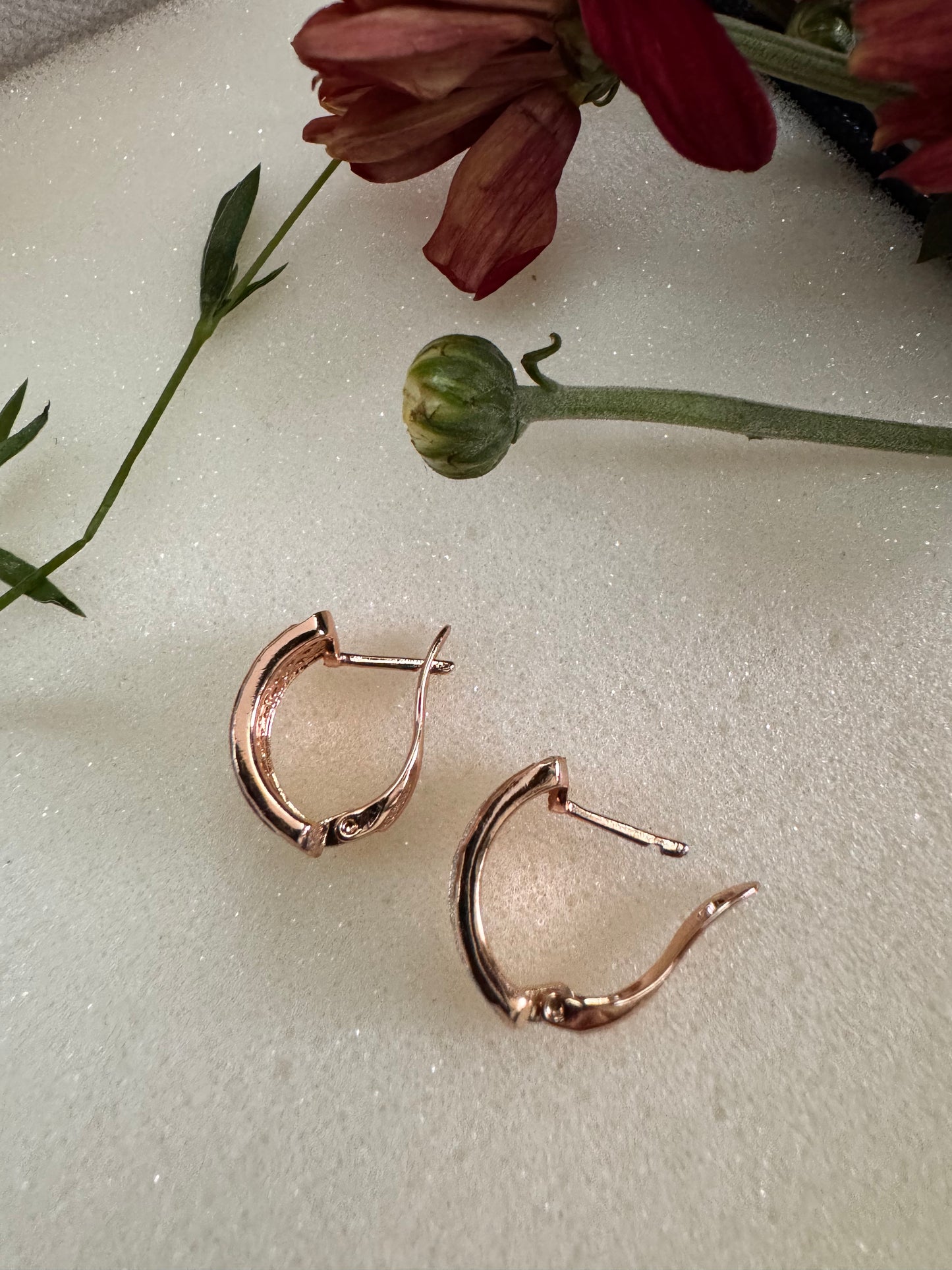 Rose gold hoop earrings on a light surface with flowers in the background. Erica Jewelry India Dainty Everyday Minimal Gold Silver Jewelry