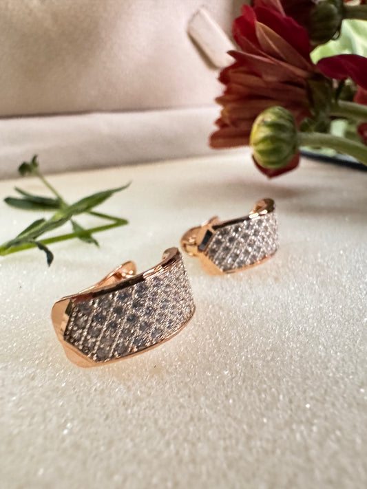 Rose gold earrings with diamond accents on a textured surface with flowers in the background
